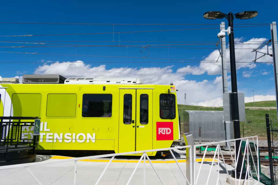 A light rail trail leaves a station with a field of grass under the blue sky in the background.